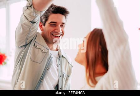Happy young couple dancing together at home, smiling man looking at woman during romantic moment in bright modern interior Stock Photo