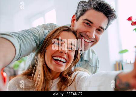 Happy young couple taking selfie together at home, smiling romantic partners making memories in bright modern living room Stock Photo