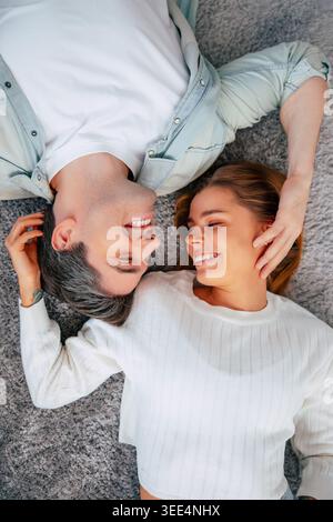 Happy young couple lying on carpet at home, romantic partners smiling and enjoying tender moment together in cozy modern living room Stock Photo