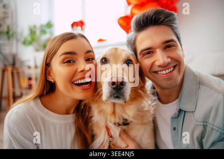 Happy young couple posing with their dog at home, smiling pet owners taking family portrait in cozy modern living room Stock Photo