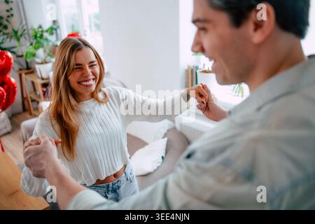 Happy young woman laughing while dancing with boyfriend at home, romantic couple holding hands in bright modern living room Stock Photo