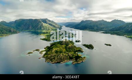Aerial drone panoramic view of tengelfjord scattered with small green forested islands surrounded by layered mountain ranges under dramatic cloudy sky Stock Photo