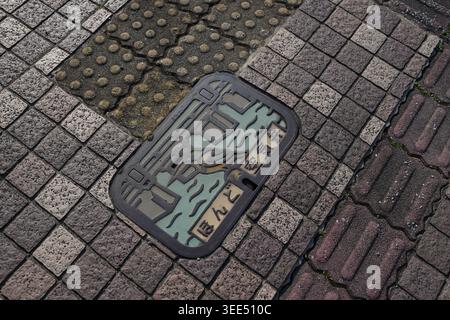 Urban scene featuring a mosaic-tiled street. Manhole cover rests among gray, brown, and beige tiles. Weathered surface shows signs of age and use. Des Stock Photo