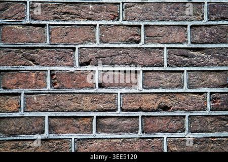Close-up straight-on view of an authentic aged brick wall with dark brown and purple tones. The rough masonry and visible grey mortar highlight histor Stock Photo