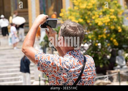 Senior man using smartphone taking photo of Thai temple, tourists using smartphone to document travel memories, rear view Stock Photo