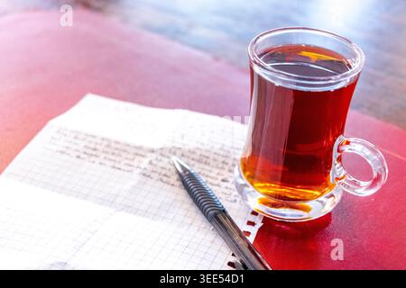 Turkish black tea chai in a glass on a restaurant table with a notepad and a pen in Patong Beach Kathu District Phuket Island Province Southern Thaila Stock Photo
