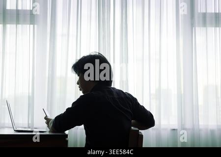 a stressed man feeling unhappy sitting with his laptop in a  small room Stock Photo