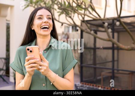 Smiling woman checking smartphone standing outside in house backyard Stock Photo