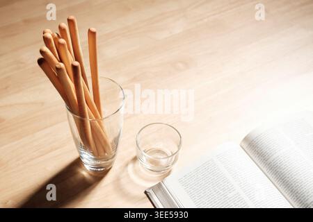 breadsticks in transparent glass with an opened page of a book on wood table Stock Photo