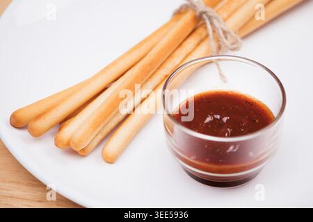 pack of breadsticks with ketchup dipping sauce in white dish on wood table Stock Photo
