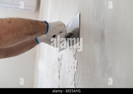 A professional contractor smoothing plaster on a wall using a stainless steel trowel. Clean construction environment with partially finished walls and visible tools in the background. Stock Photo