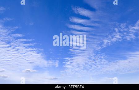 Fluffy clouds across bright blue wallpaper sky. Clean blue air with scattered clouds. Gentle light over the horizon sky line. Abstract cloud texture Stock Photo