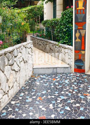 Mosaic garden path in Nizza, France with stone walls and lush greenery. Colorful tiled walkway leading through a Mediterranean residential entrance Stock Photo