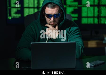 Hacker types code with concentration. Hacker analyzes network security system. Hacker monitors online data transmission. Hacker executes phishing Stock Photo