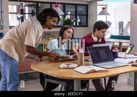 Diverse students leaning, pointing and working together at modern lounge with laptops and open book Stock Photo