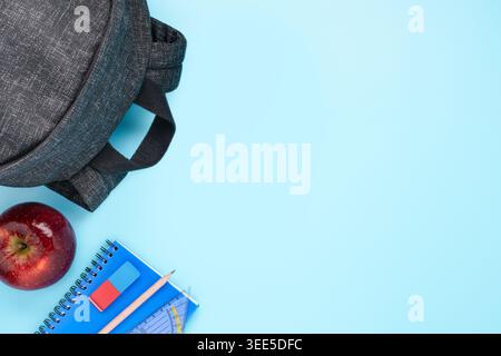 school supplies set backpack apple notebook and stationery on blue background copy space Stock Photo