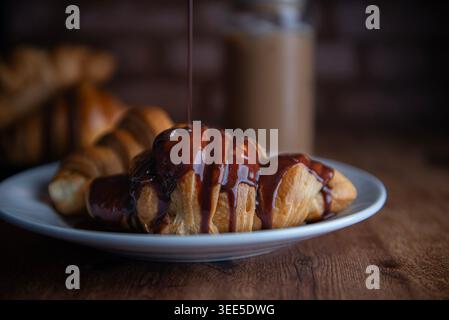 Pastry shop or bakery, puff pastry covered with dark chocolate, on a white plate, with cold coffee or frappe in the background Stock Photo