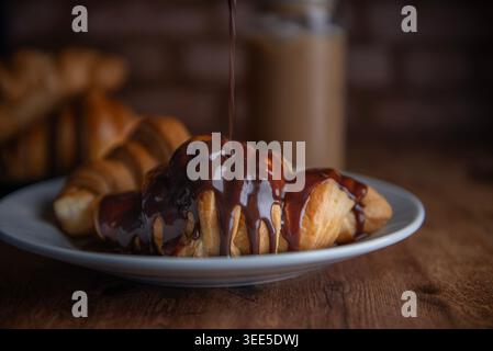 Pastry shop or bakery, puff pastry covered with dark chocolate, on a white plate, with cold coffee or frappe in the background Stock Photo