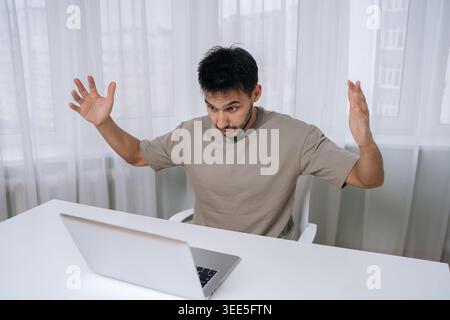 Confused bearded man reacting with shock and frustration, seeing bad online news or notification on laptop, feeling stressed and overwhelmed by unexpe Stock Photo
