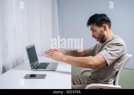 Side view of frustrated man reacting to shocking problem on laptop, experiencing stress, burnout, mistake and error during remote work at home desk. Stock Photo