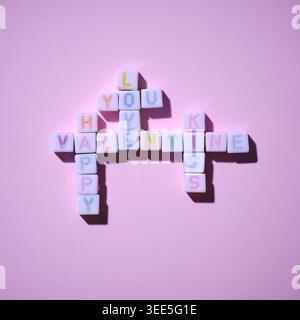 crosswords of colorful alphabet blocks in the words of love, you, kiss, happy, valentine on textured pink paper. Stock Photo
