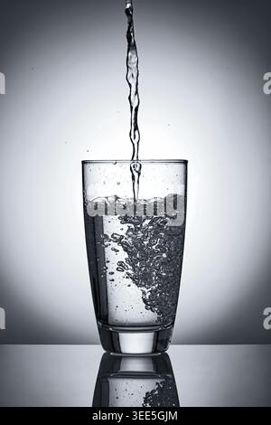 puring refreshment freshness drinking water to a half clean transperence glass of water with many splashing bubbles in studio back light. Stock Photo
