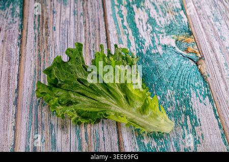 A single fresh green lettuce leaf lies on a rustic, weathered wood table with peeling turquoise paint. The minimalist composition, shot from above, hi Stock Photo