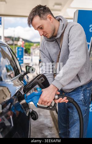 Young man filling black vehicle with gasoline at modern fuel station during everyday driving and transportation activity Stock Photo