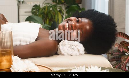 Relaxed Young Woman Receiving Spa Treatment on Massage Table Smiling in Bright Wellness Room Stock Photo