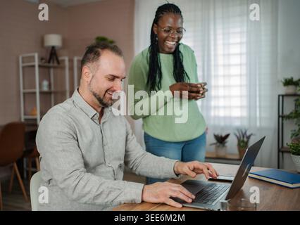 Happy multicultural couple collaborating and laughing while working remotely at home Stock Photo