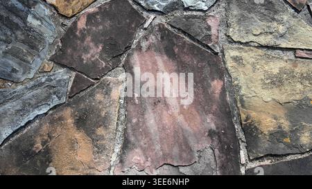 Close up of flat slate stones set in thick, porous, uneven mortar joints with varied stone colors, shapes, and sizes Stock Photo