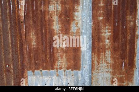 Close up of rusted overlapping corrugated tin panel siding showing vertical ridges, corroded rust patterns, worn silver metal areas Stock Photo