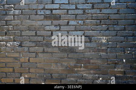 Painted black brick wall with smooth and rough bricks that are cracked, uneven, and chipped Stock Photo