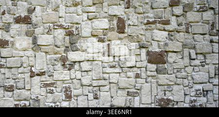 Stone wall surface with light gray, painted brown, and darker gray rectangular stones in various sizes Stock Photo