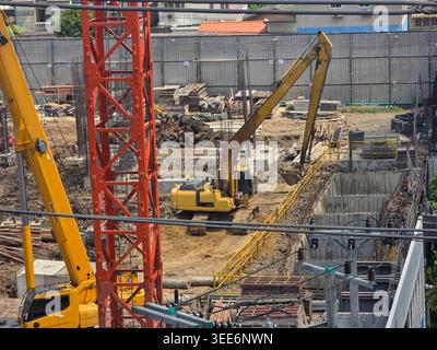 Active construction site featuring heavy machinery yellow excavator digging dirt near red crane foundation trench bustling industrious progress enviro Stock Photo