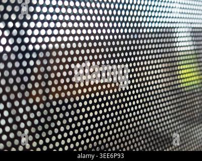 Close macro view of perforated mesh hole dot pattern texture creating an abstract background. Light shines through dark surface evoking calm mysteriou Stock Photo