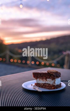 A delicious piece of chocolate layer cake with white cream served on a small plate outdoors Stock Photo