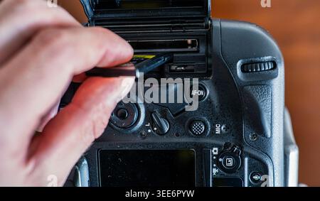Close-up of a photographer inserting a memory card into a professional DSLR camera slot Stock Photo