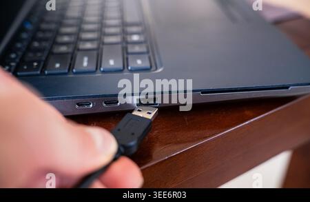 Close-up of a person connecting a black USB type A cable into a laptop port Stock Photo