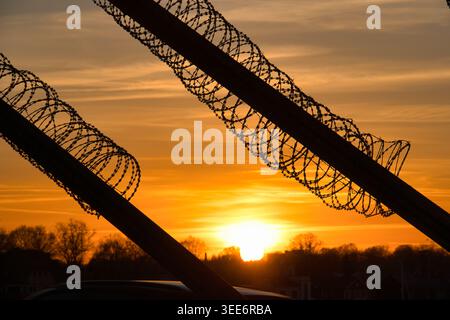 Razor Wire Security Fence Silhouette Against Dramatic Orange Sunset Sky Stock Photo