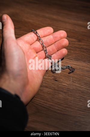 Hand holding a small metal chain over a wooden background Stock Photo