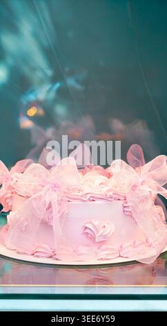 Elegant pink frosted cake decorated with sheer fabric bows in a display case Stock Photo