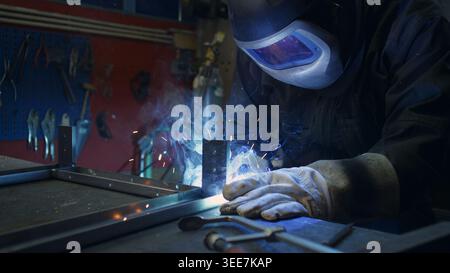 Worker wearing a protective helmet and gear during the welding process in the workshop, making metal construction. Stock Photo