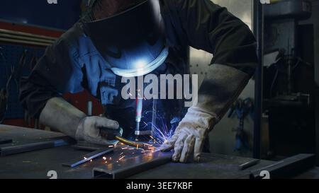Skilled welder worker with experience in metal fabrication, using MIG welding techniques to create sparks and shape metal components. Stock Photo