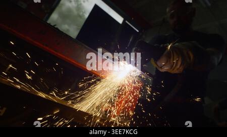 Worker operating a plasma cutter, cutting metal and producing bright sparks in a dark workshop. Job, work and craft concept. Stock Photo