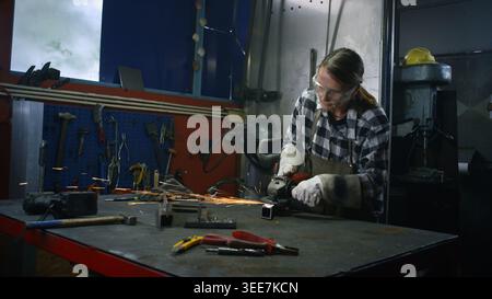 Woman mechanic working in a small home business metalworking workshop, grinding steel with circular saw. Economy and employment concepts. Stock Photo