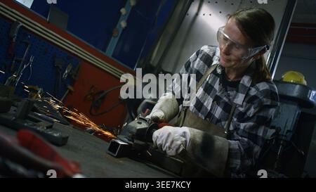Female worker wearing protective equipment grinding steel in a welding workshop. Women in metalwork industry career concept. Stock Photo