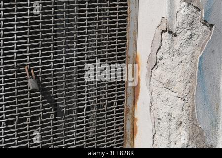 RUSTY METAL GRID TEXTURE BACKGROUND WITH A FRAGMENT OF RUINED AND PEELING URBAN WALL Stock Photo