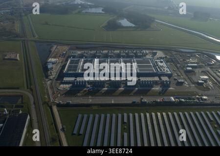 Aerial view of an AI data center with cooling towers and a cloud computing hub exterior featuring a blue industrial building, solar panels and green f Stock Photo