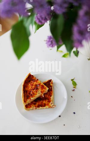 Delicious baked pie served near blooming lilac flowers in bright modern interior with soft natural daylight. Stock Photo